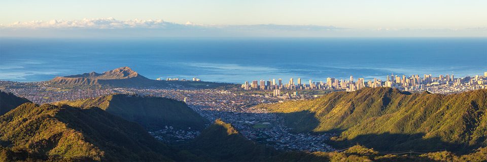 View from a ridge above Pālolo Valley across Honolulu to Diamond Head and the Waikīkī skyline at golden hour