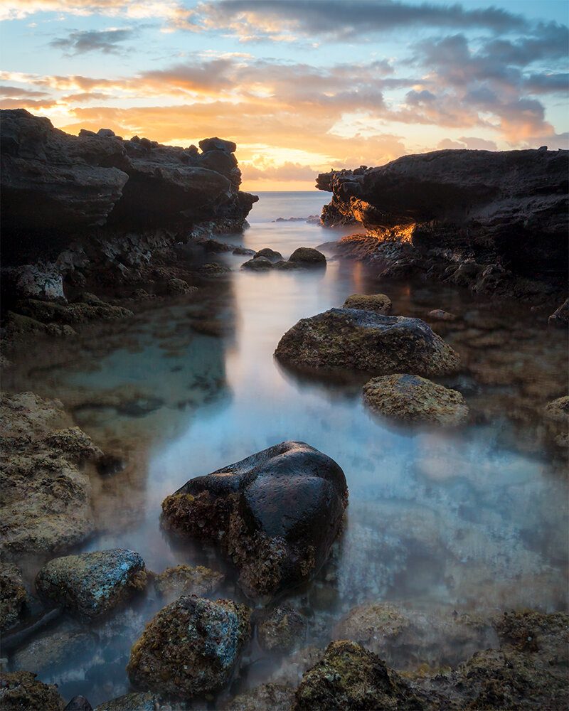 Long exposure of a tide pool on the Kaiwi coast, smooth frosted water between dark lava rocks at sunrise