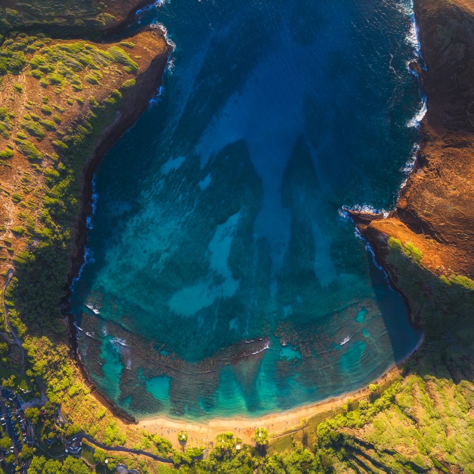 Aerial view straight down into Hanauma Bay at sunrise, the reef showing through clear blue water inside the crater