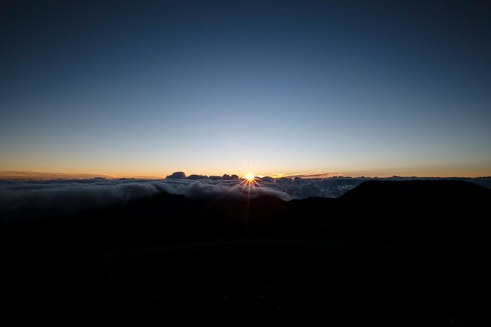 The first light of sunrise breaking over a sea of clouds from the summit of Haleakalā, Maui