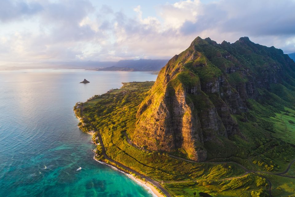 Aerial view of the Kaʻaʻawa Valley ridge at sunrise, green cliffs dropping toward the coastal highway and turquoise water
