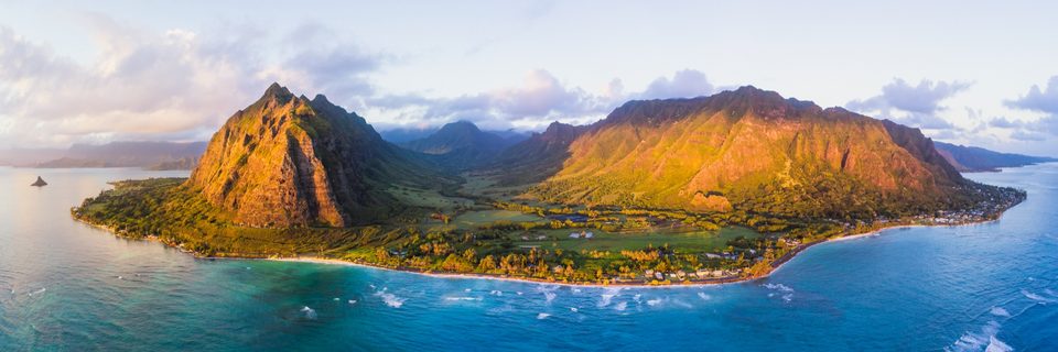 Aerial panorama of Kaʻaʻawa Valley and the Kualoa ridges, with Mokoliʻi offshore and clouds over the mountains