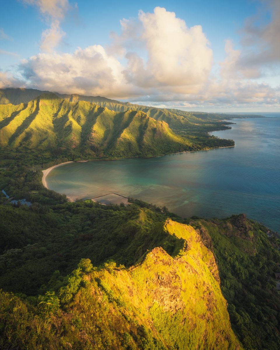View from a ridge above Kahana Bay at sunrise, the valley and beach curving below