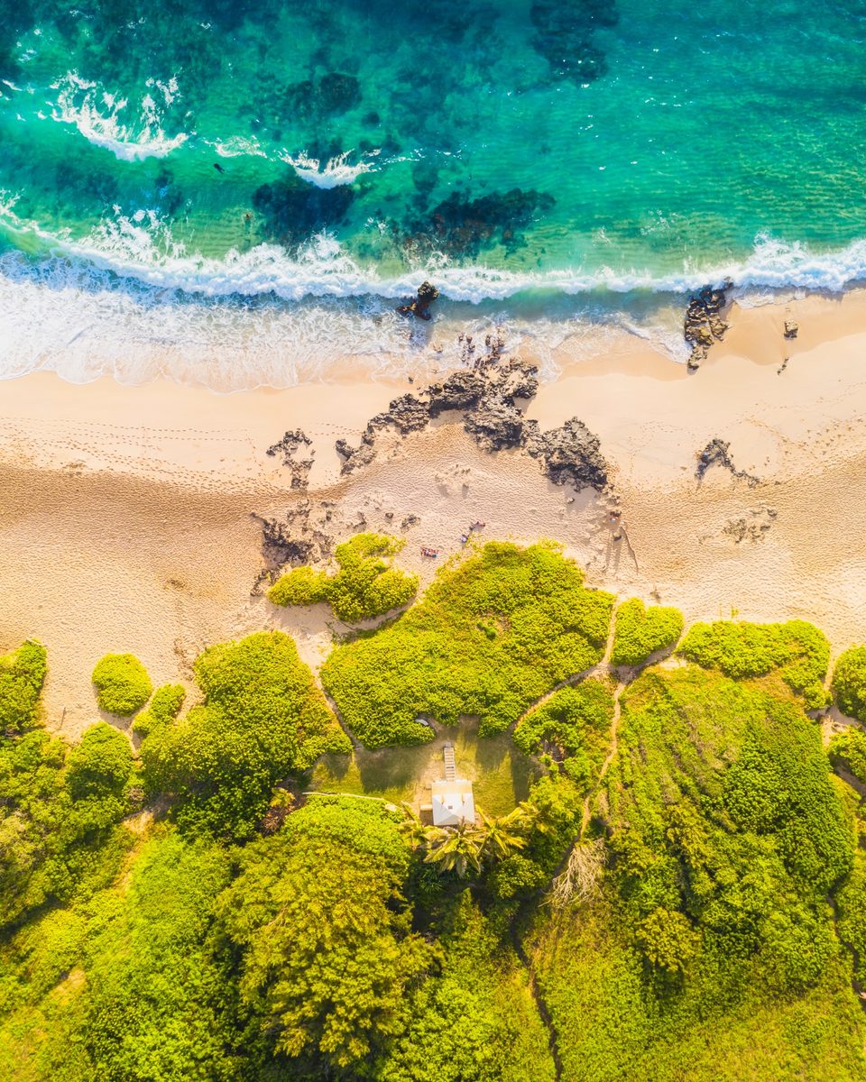 Straight-down aerial of Makapuʻu Beach, turquoise water above white sand and green naupaka