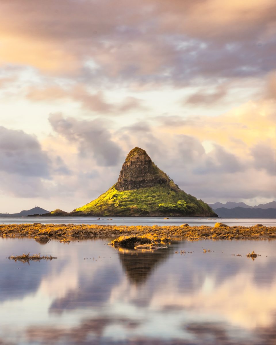 Mokoliʻi islet at sunrise, reflected in still water over the low tide reef