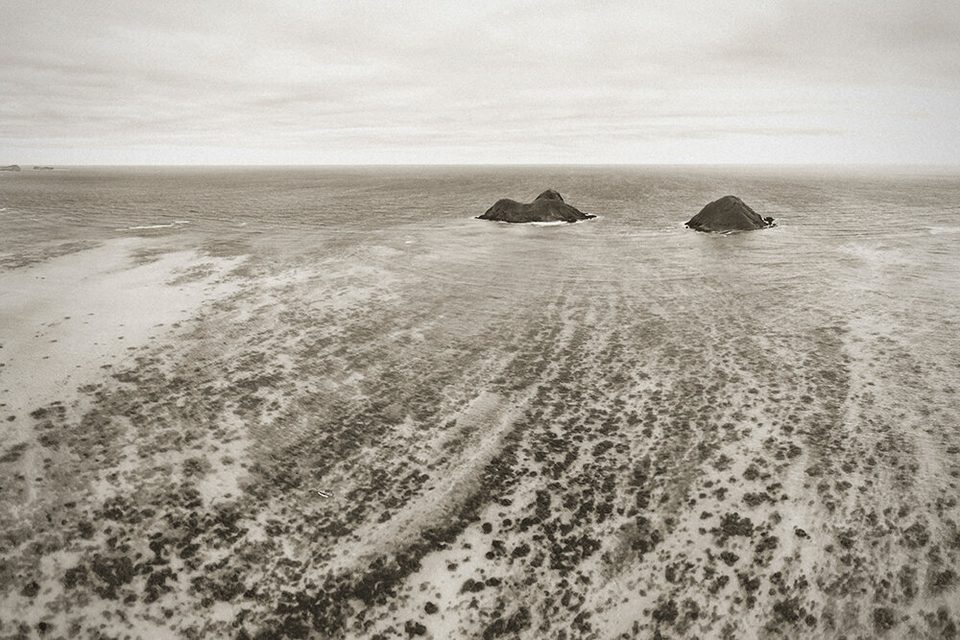 Black and white aerial of the two Mokulua islets off Lanikai, reef lines in the sand leading out to them