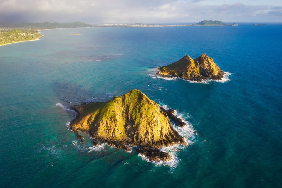 Aerial view of the two Mokulua islets off Lanikai in warm low light, turquoise water and the Kailua coast behind them
