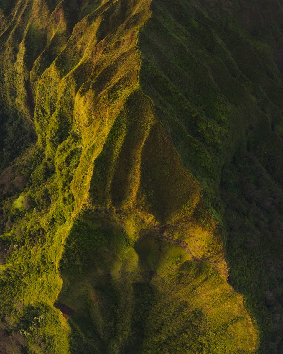 Aerial view of a triangular face of the Koʻolau Mountains, lush ridges lit from one side