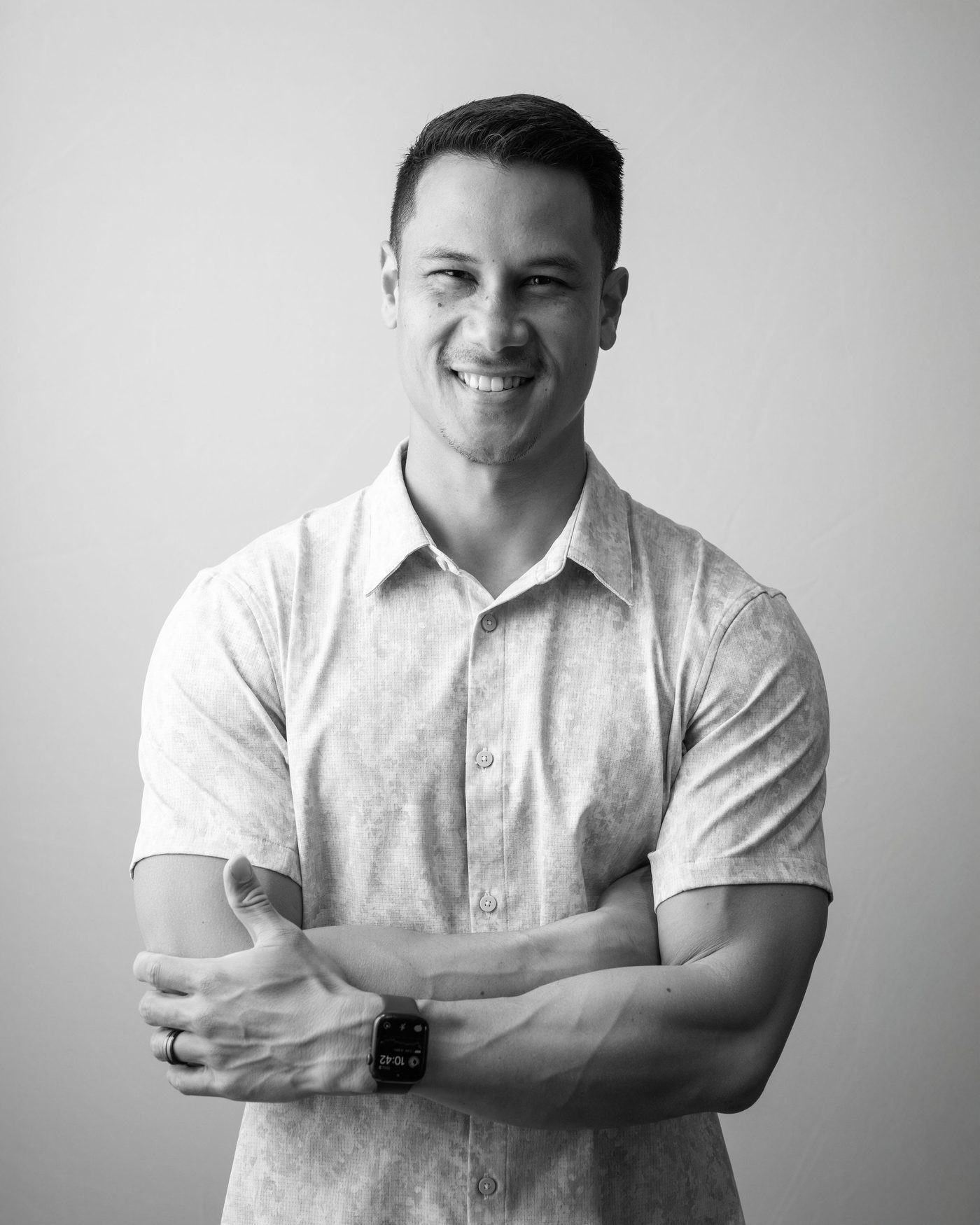 Kawika Lopez, smiling with his arms crossed, in a black and white portrait